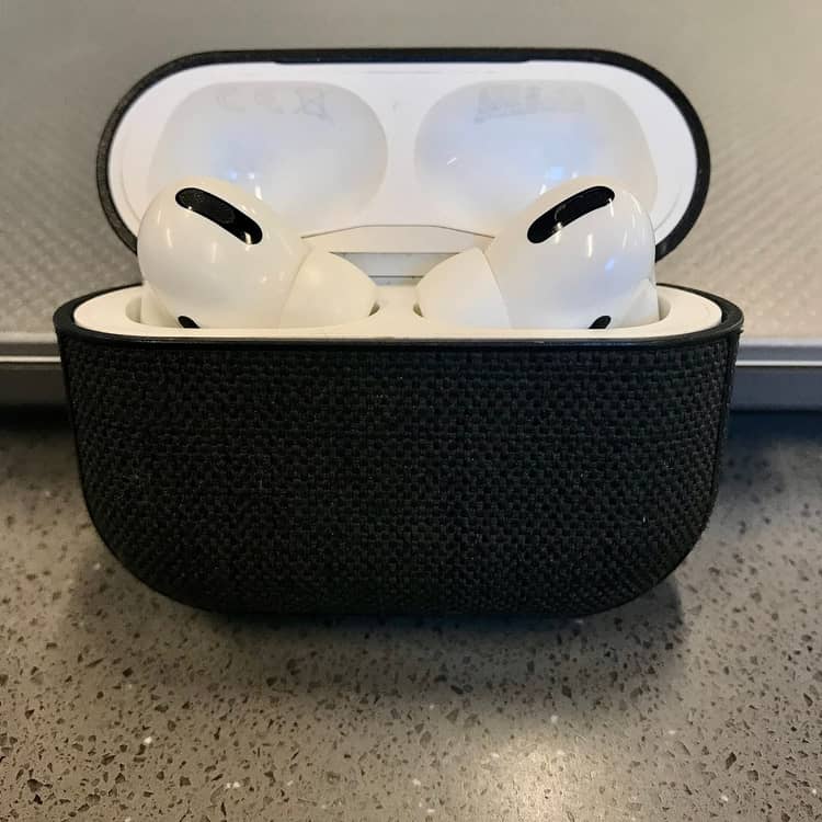 AirPods Pro seated in an open case with a black fabric sleeve on a counter